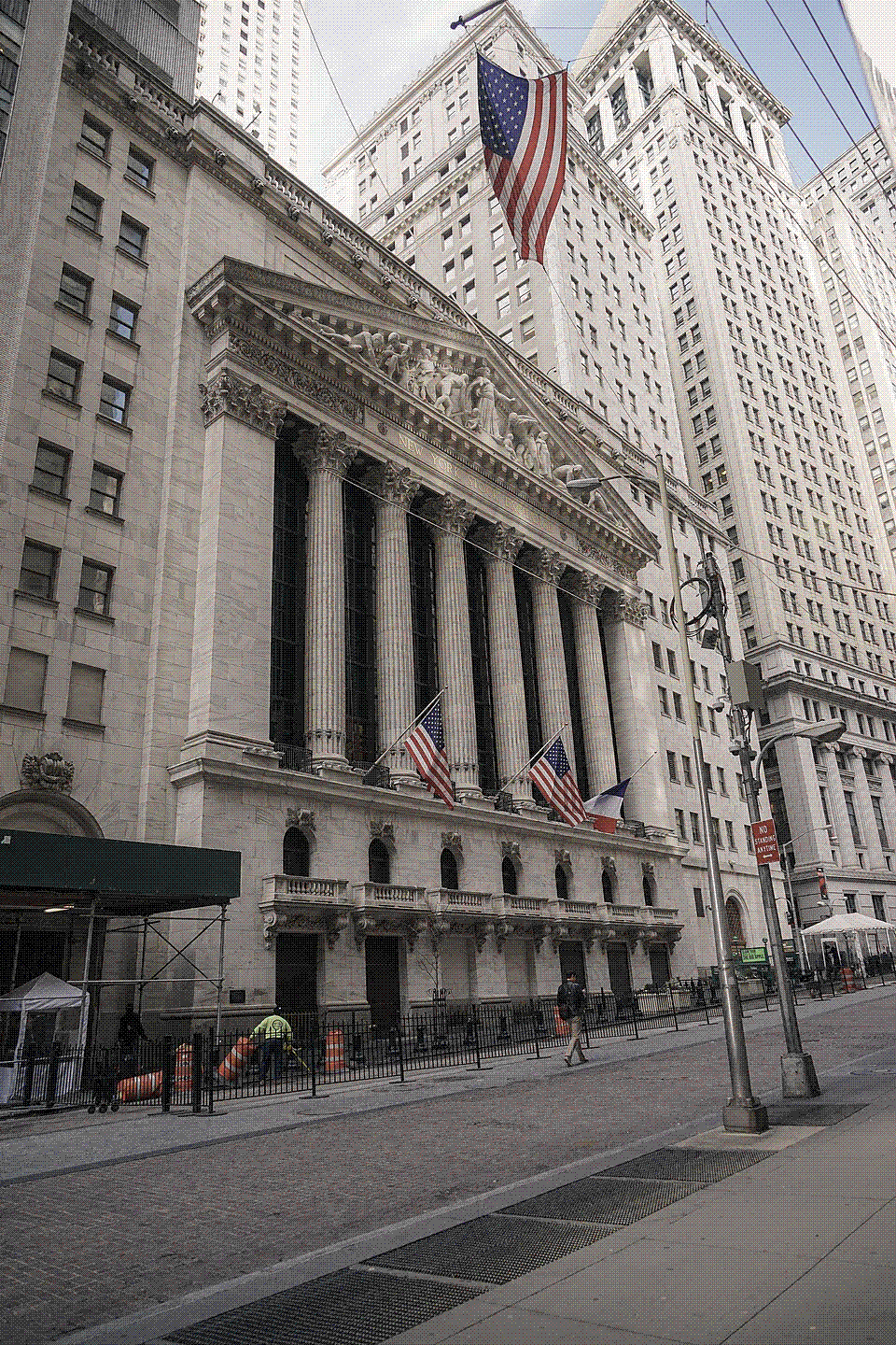 The columned neoclassical Wall Street facade of the New York Stock Exchange building, draped with a large flag.