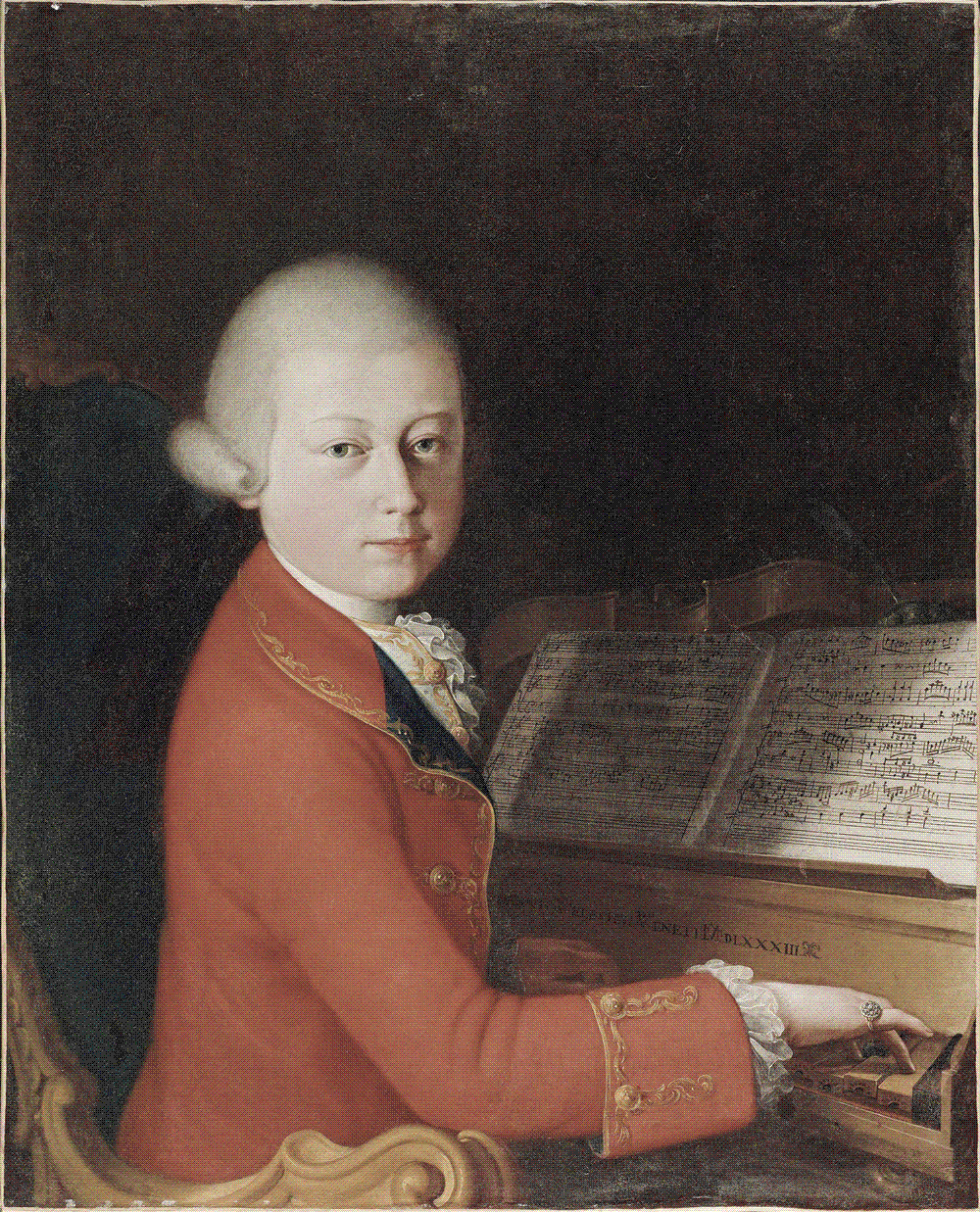 A pale boy in a gold-braided scarlet coat and powdered wig sits at a small keyboard instrument, one hand on the keys, an open manuscript of music propped on the stand, turning his head to look out at the viewer.