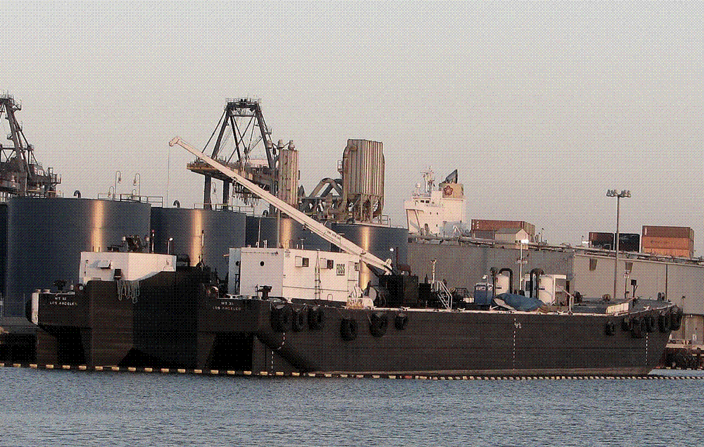 Rows of stacked shipping containers and a gantry crane at a busy port terminal handling imported goods.