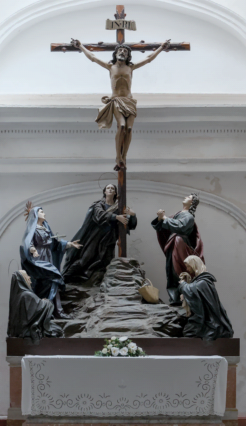 The dim lower chapel of the Oratorio de la Santa Cueva in Cádiz: a low subterranean vault of dark stone with a carved crucifix above a small altar, lit by a single hanging lamp.
