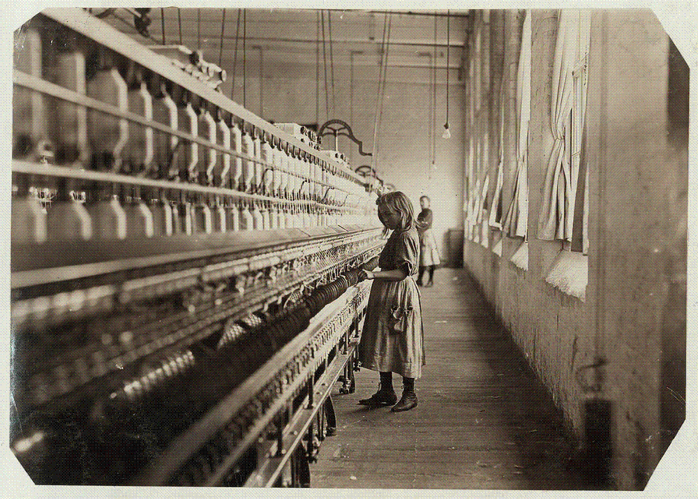 A small girl, Sadie Pfeifer, stands dwarfed by the long row of spinning frames she tends in a South Carolina cotton mill, 1908.