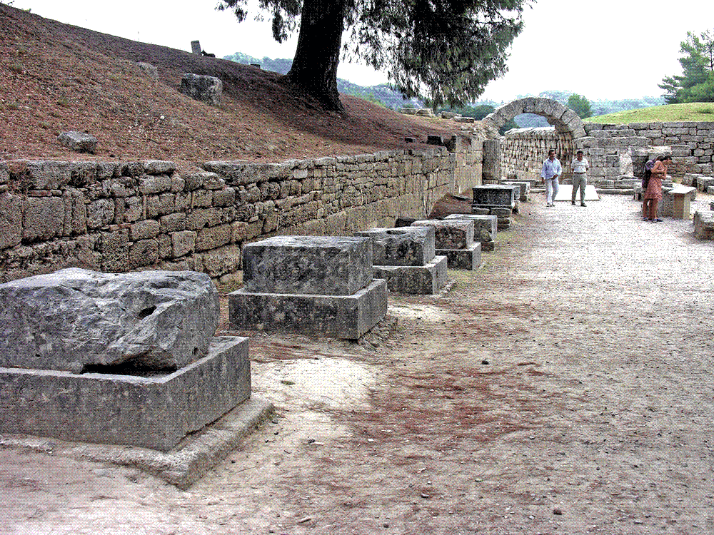 Row of stone statue bases (the Zanes) lining the entrance to the ancient stadium at Olympia, funded by fines levied on athletes who bribed their way to victory