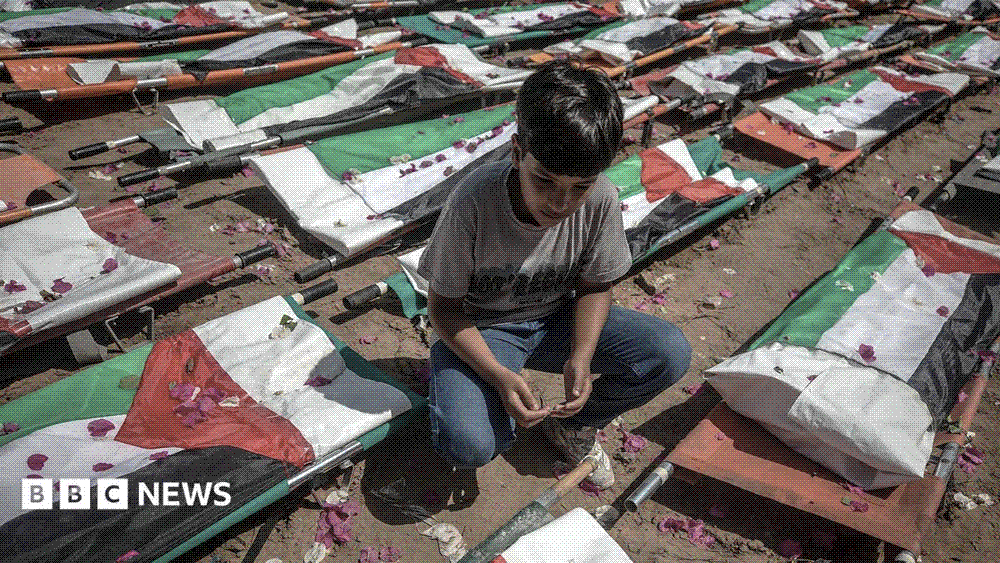 A boy crouching beside rows of stretchers draped in Palestinian flags at the mass funeral in Gaza City.