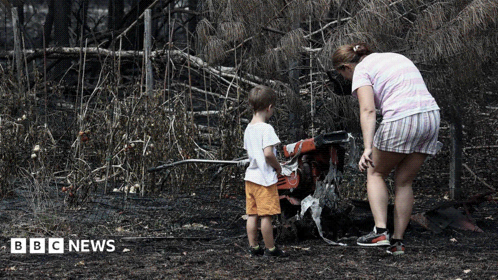 A mother and son standing in the burnt-out surroundings of their destroyed home in Le Porge after the Gironde wildfire.