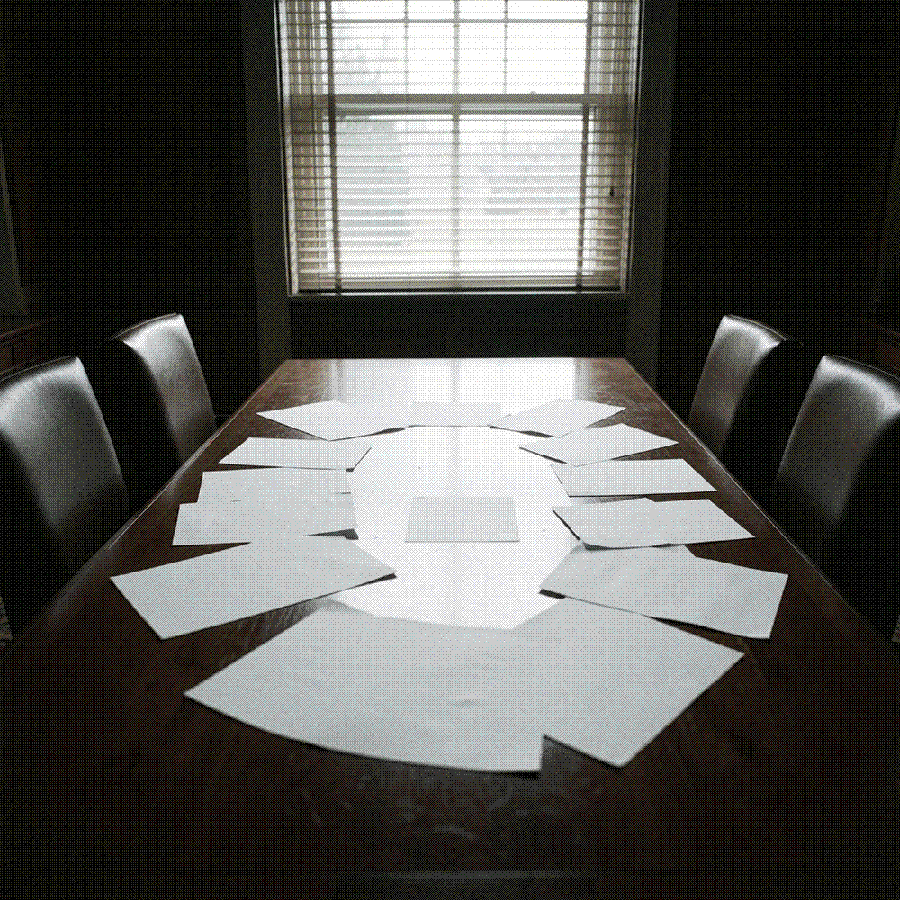 Long empty negotiating table with fifteen blank pages fanned across it and two heavy chairs pushed back